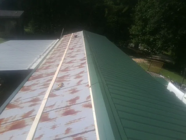 Old rusted panels beside newly installed green metal roofing — Wind Damage Roof Repair by Roofing Brothers in Freeport