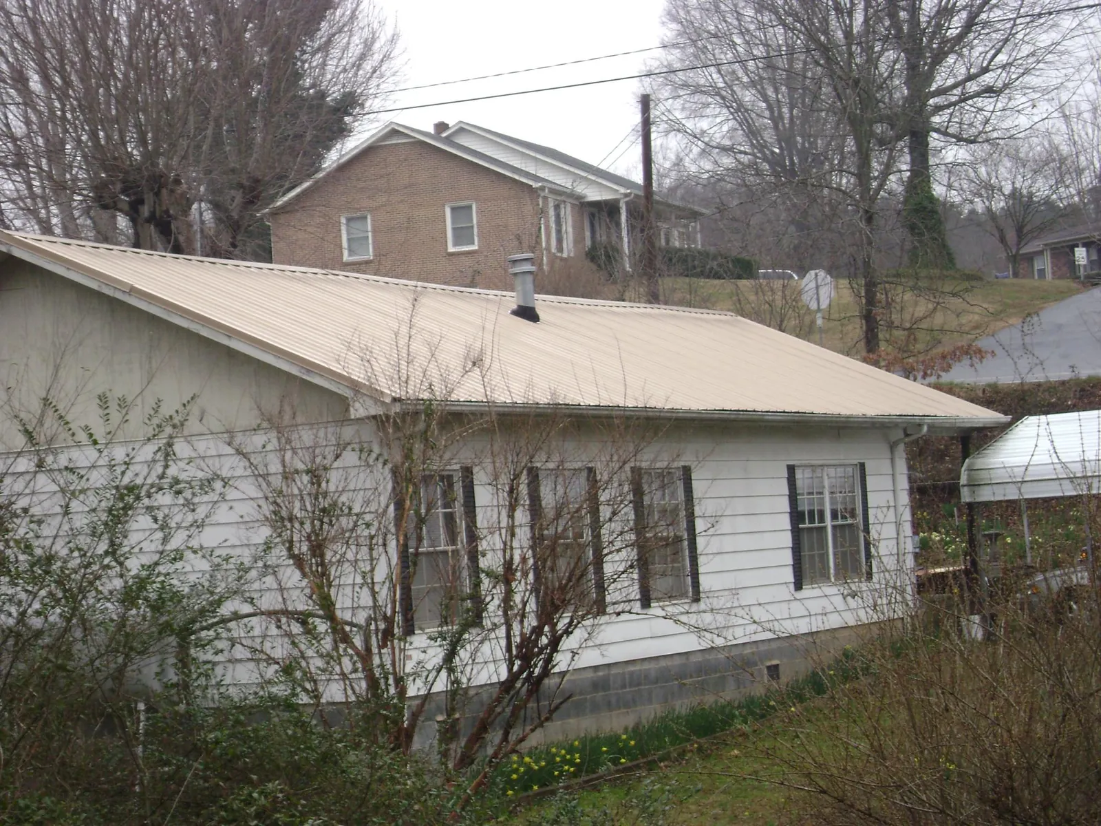 Tan metal roof on a white sided house set into a hillside — Commercial Roofing by Roofing Brothers in Freeport